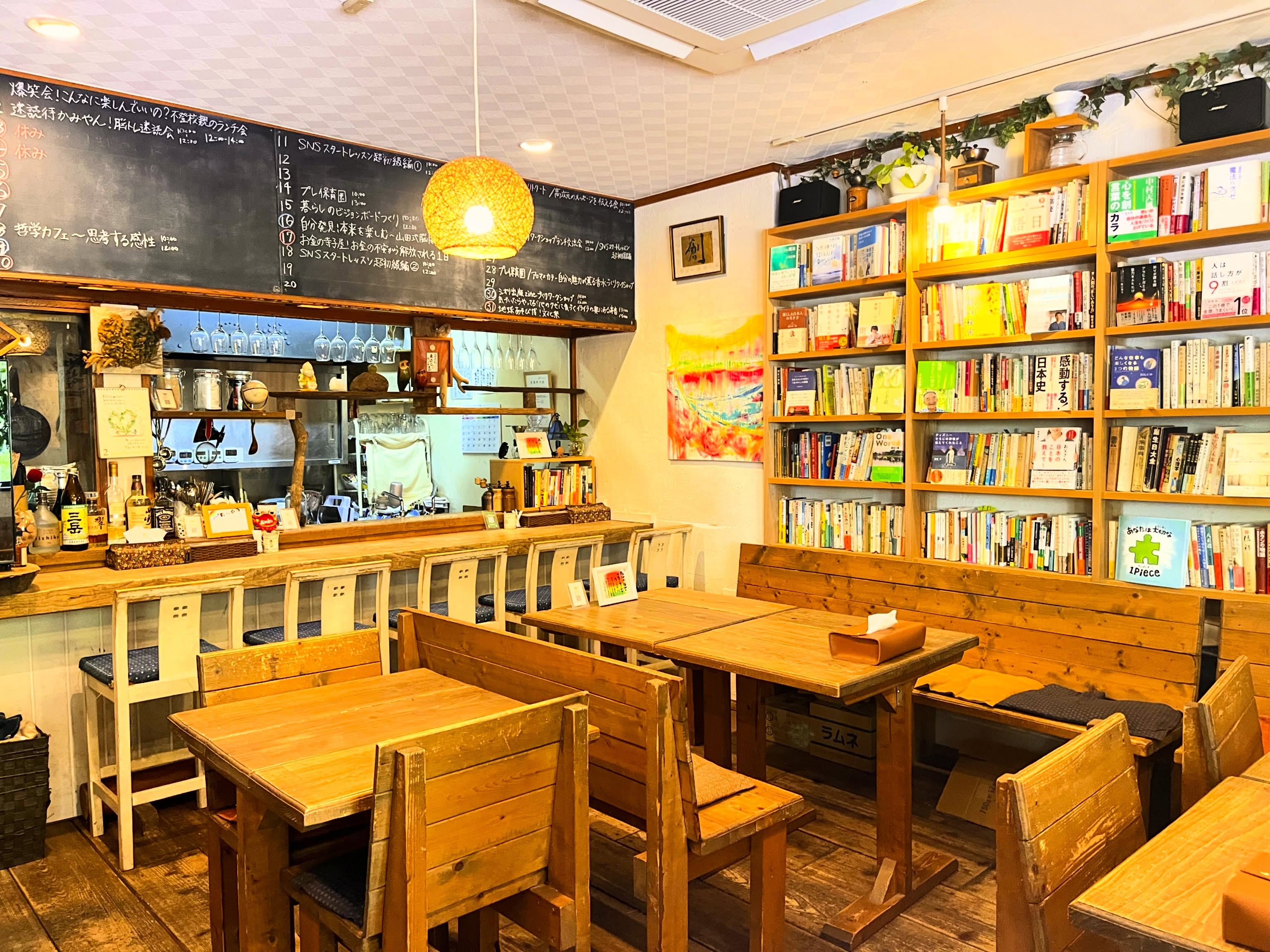 アサカフェの店内。黒板に書かれた多彩なイベント予定と、壁一面の本棚に囲まれた木のテーブル席